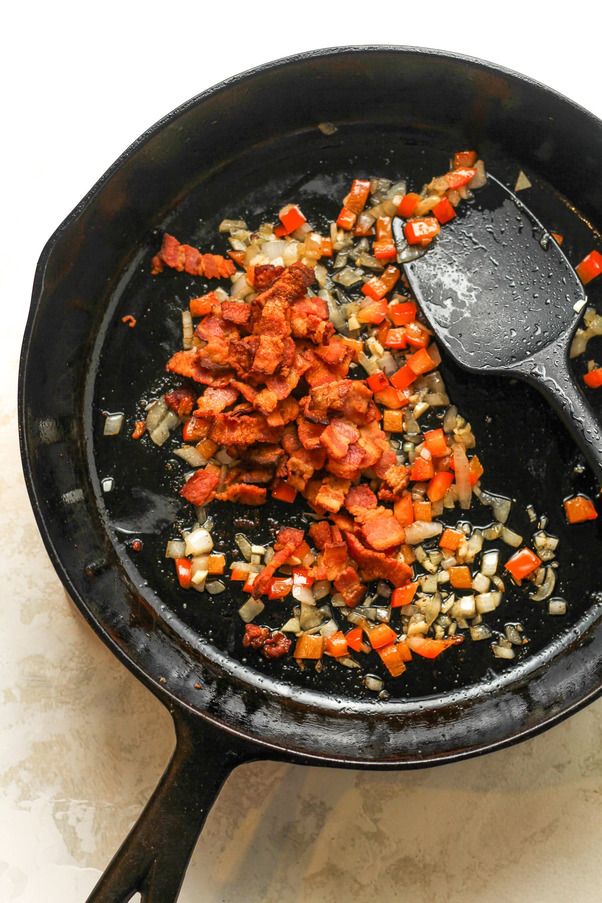 A cast iron skillet of the sautéed onion, bell peppers, and bacon.