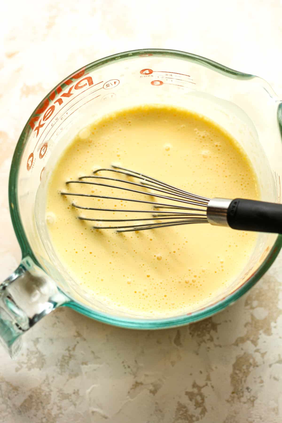 A measuring cup with eggs and heavy cream with a whisk.