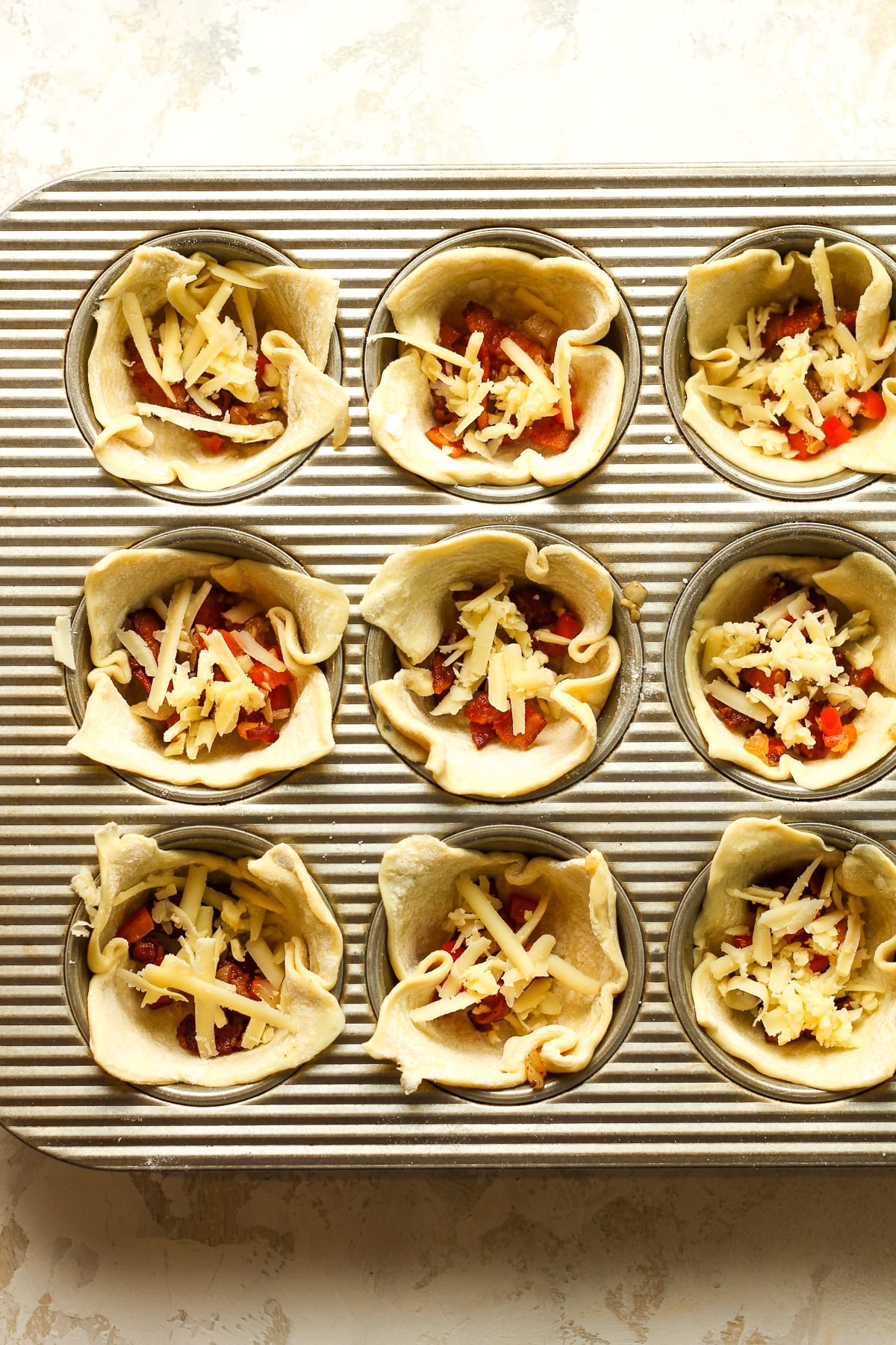 A muffin tin with the puff pastry, bacon, veggies, and cheese.