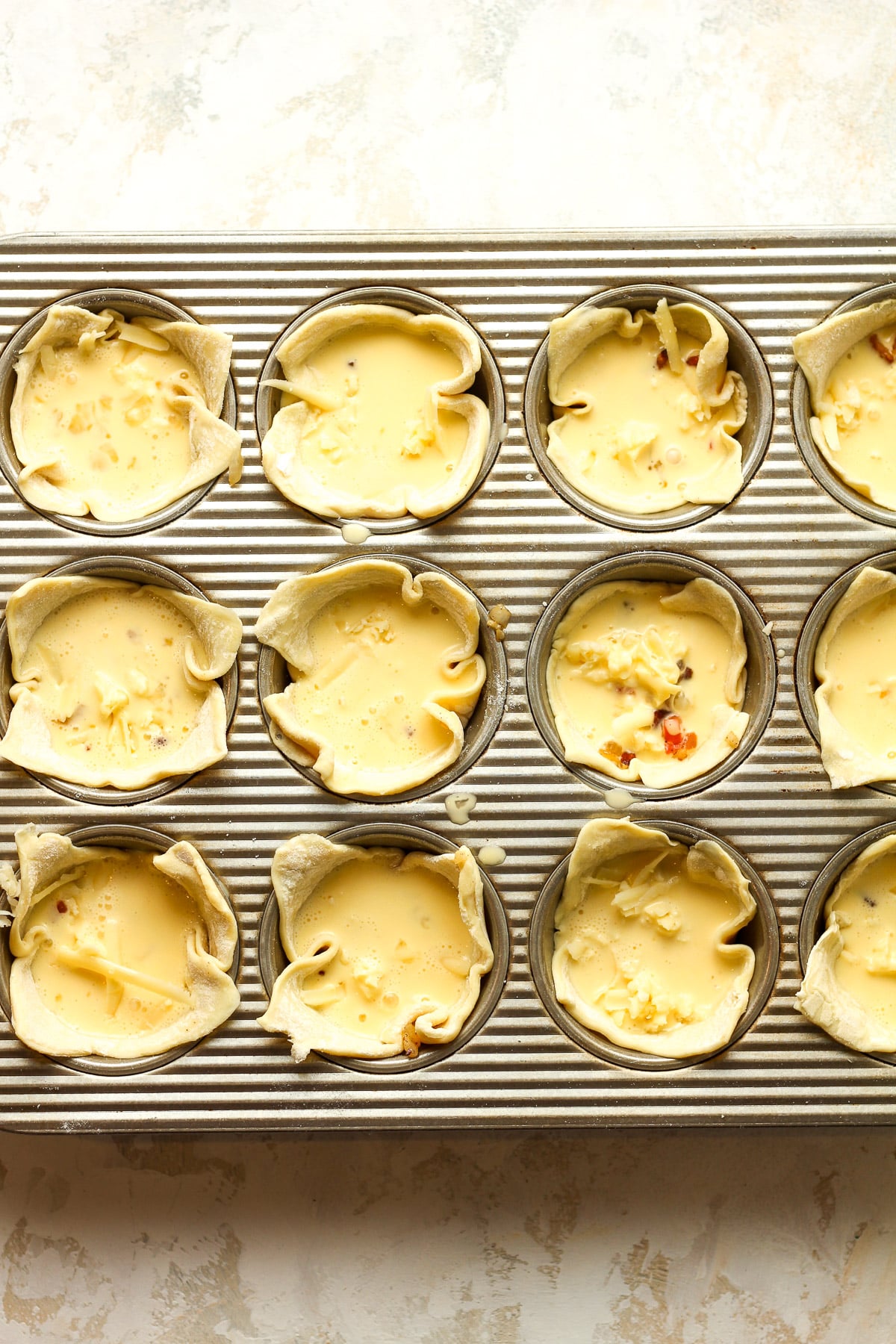 A cupcake pan with the puff pastry and ingredients before baking.