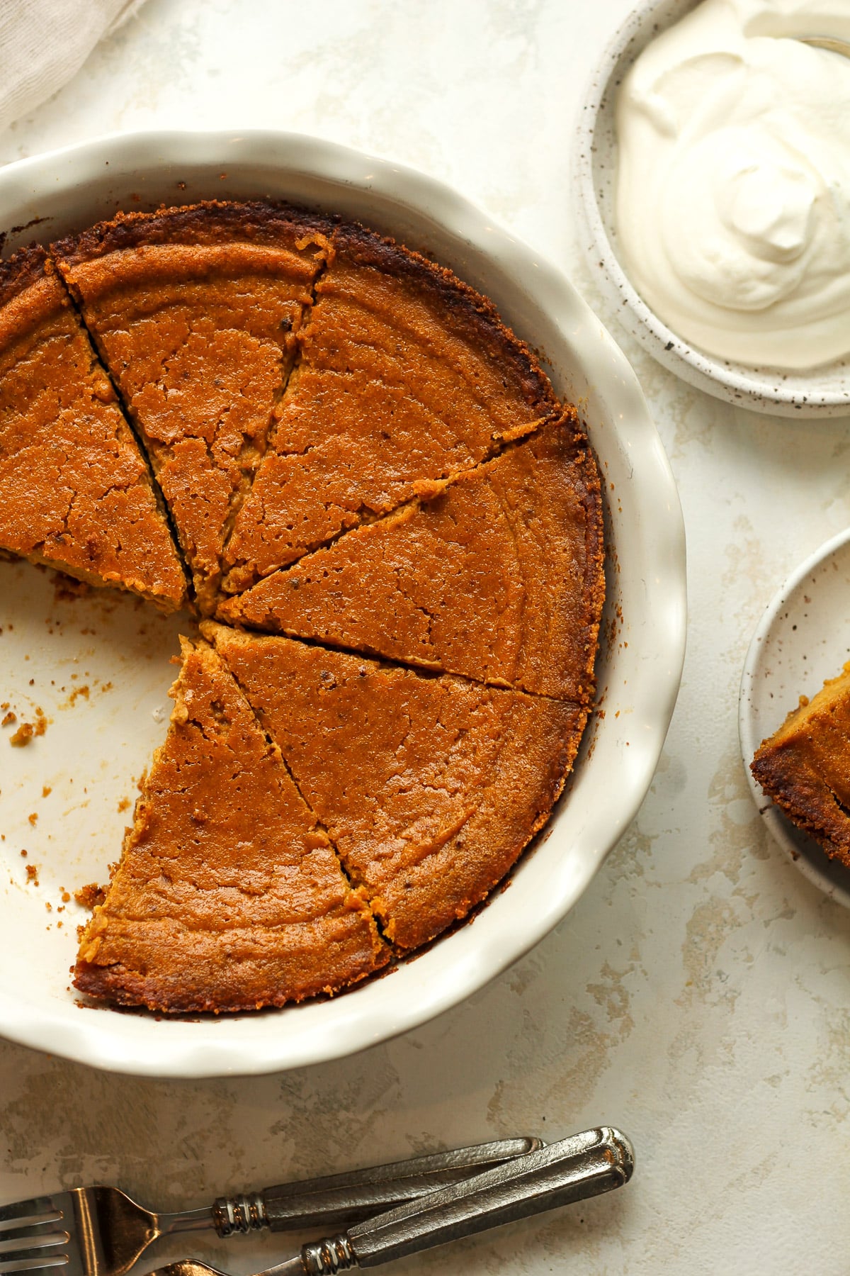 Overhead shot of a pumpkin pie in graham cracker crust with a small bowl of whipped cream.