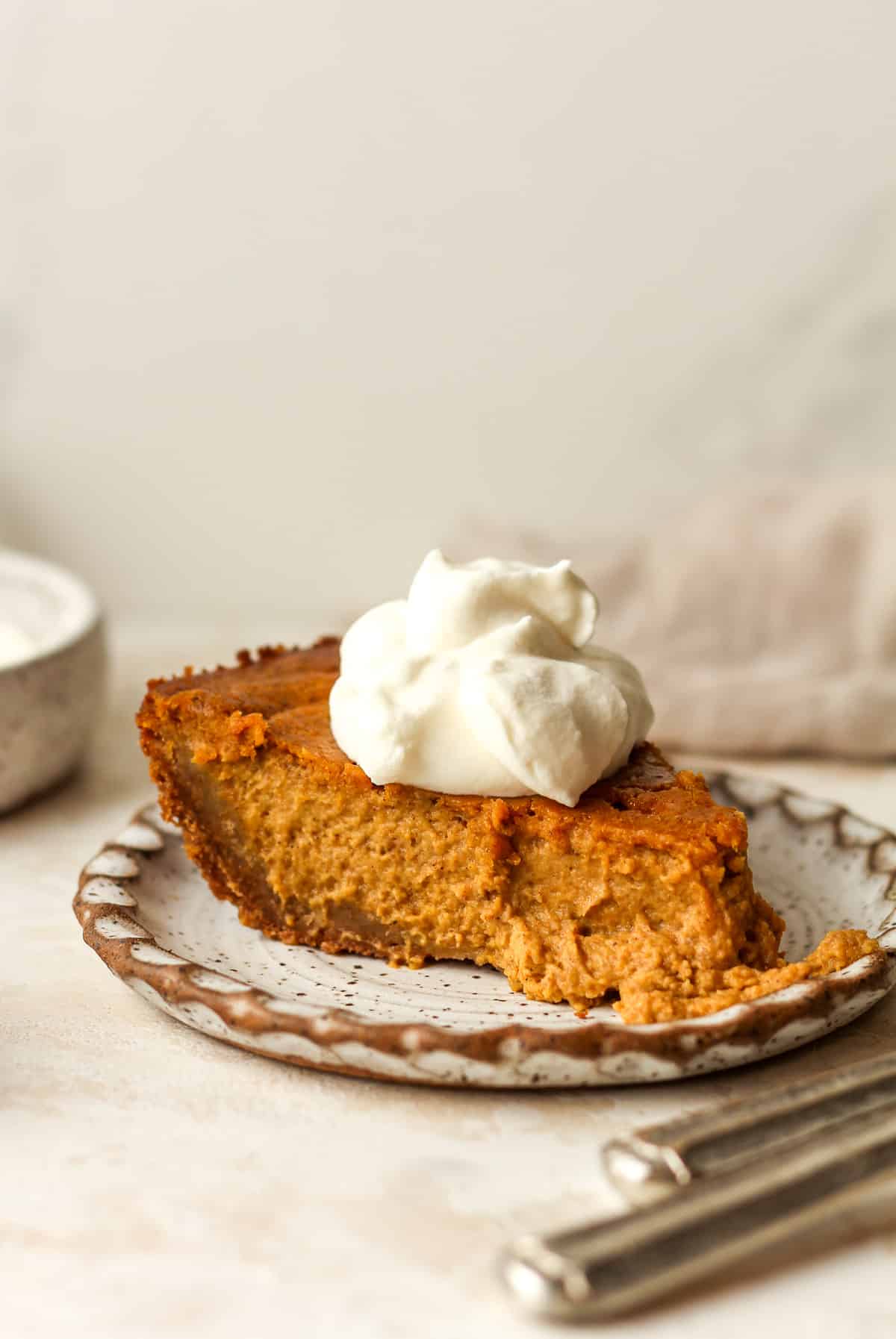 Side view of a slice of pumpkin pie in a graham cracker crust with a dollop of whipped cream.