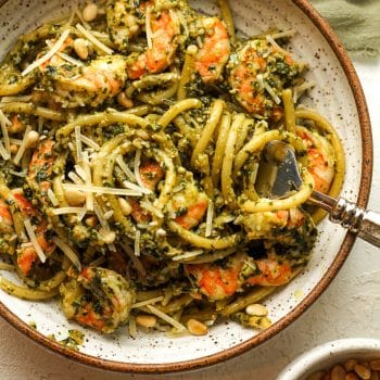 Closeup on a bowl of shrimp pesto pasta with a fork swirling the noodles.