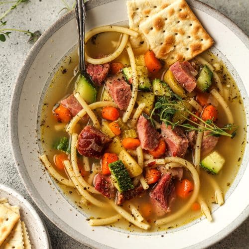 A shallow bowl of veggie soup with leftover ham and crackers.