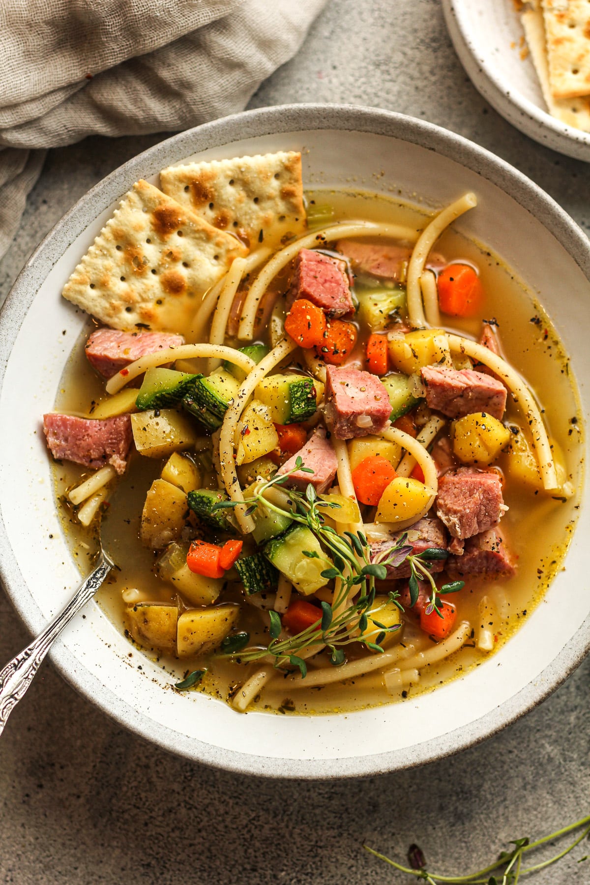 Overhead view of a bowl of veggie soup with ham and noodles.