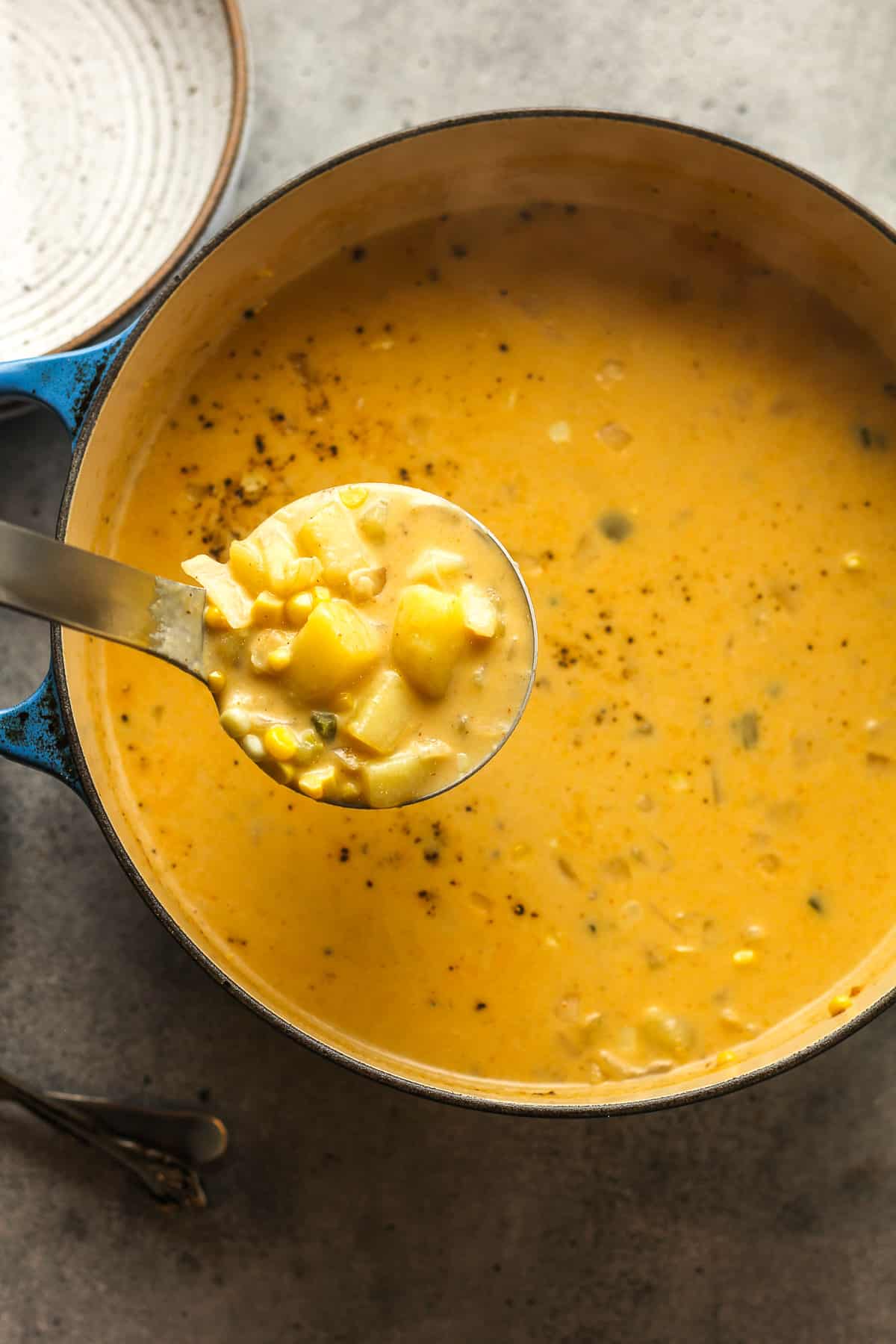 A stock pot of street corn chowder with a ladle lifting some out.