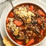 A bowl of beef barley soup with ritz crackers.