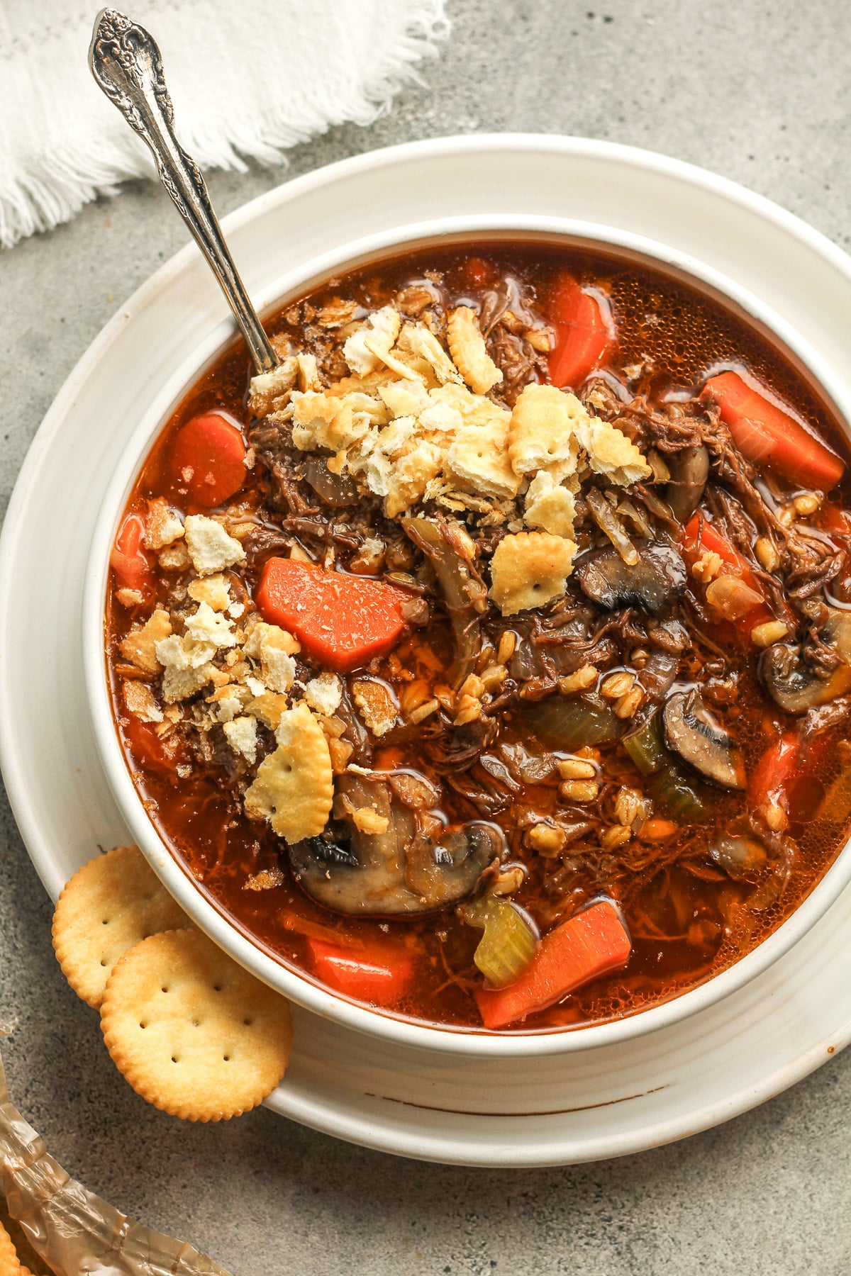 A bowl of beef barley soup with crushed ritz crackers.