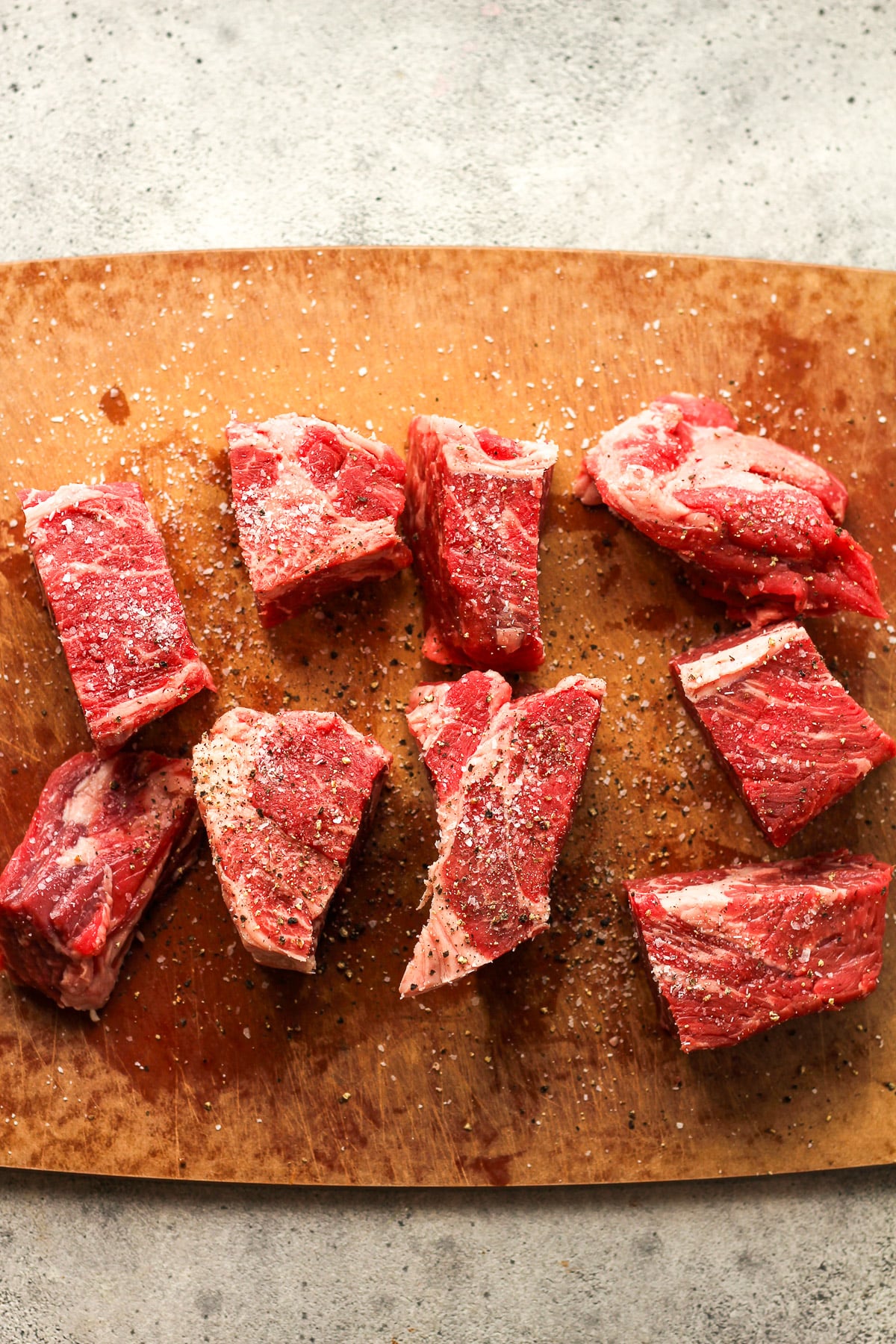 A cutting board of the beef chunks with salt and pepper.