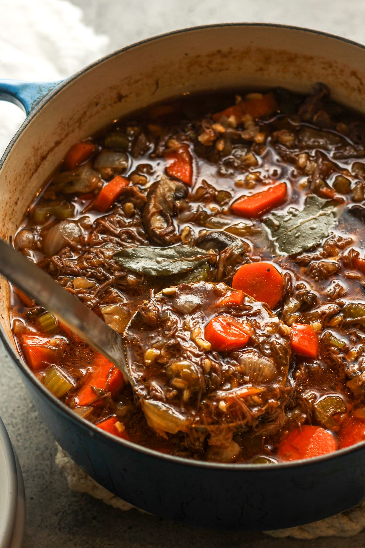 A large pot of beef barley soup with a soup ladle lifting some up.