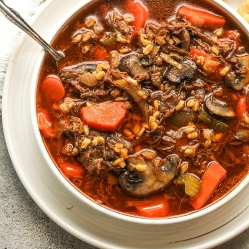 Closeup on a bowl of beef barley soup with ritz crackers.