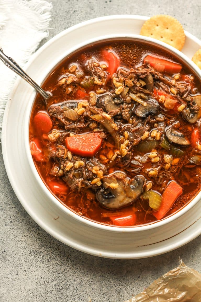 Closeup on a bowl of beef barley soup with ritz crackers.