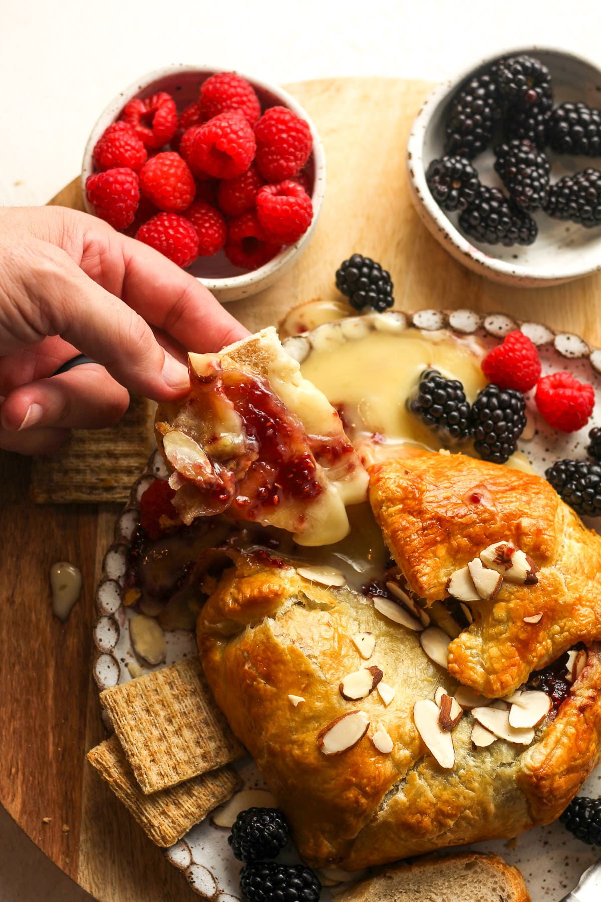 A hand holding out some bread topped with puff pastry, brie, and jam.