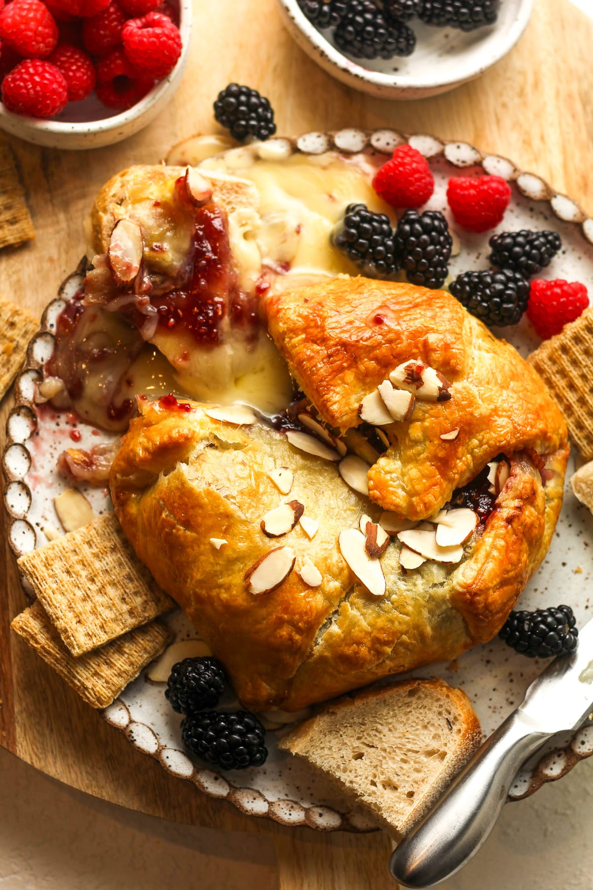 Overhead view of bridge and jam puff pastry with bread, crackers, and berries.