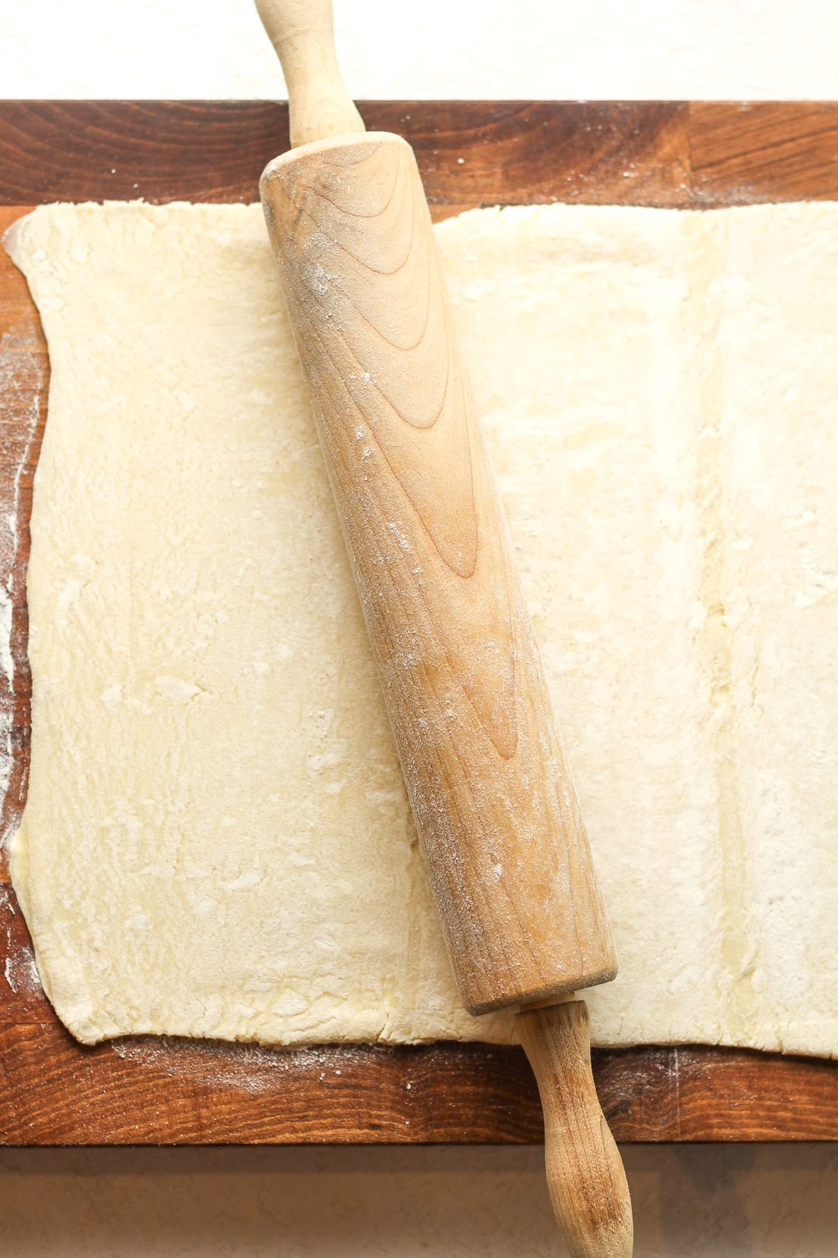 A board with puff pastry and a rolling pin on top.