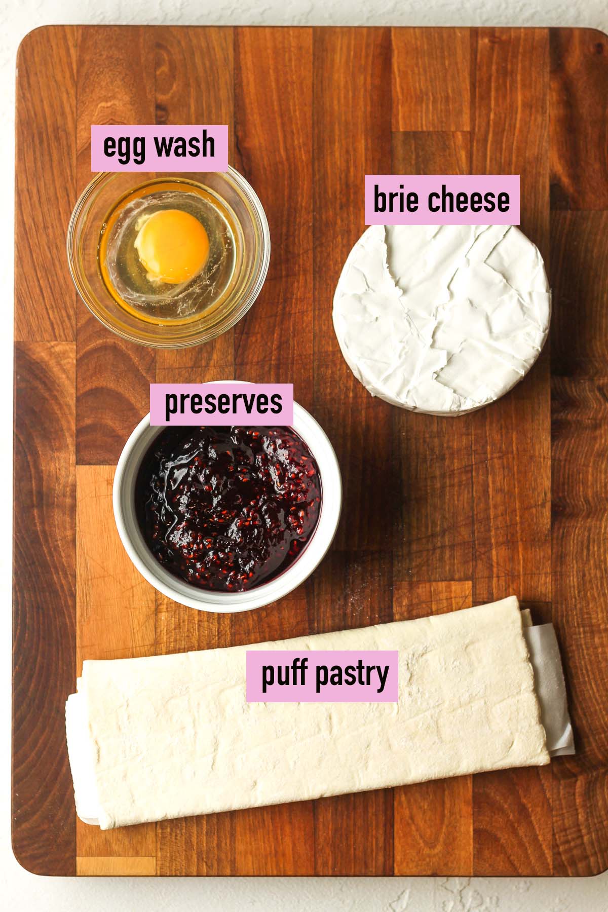 A board with four labeled ingredients for brie and jam in puff pastry.