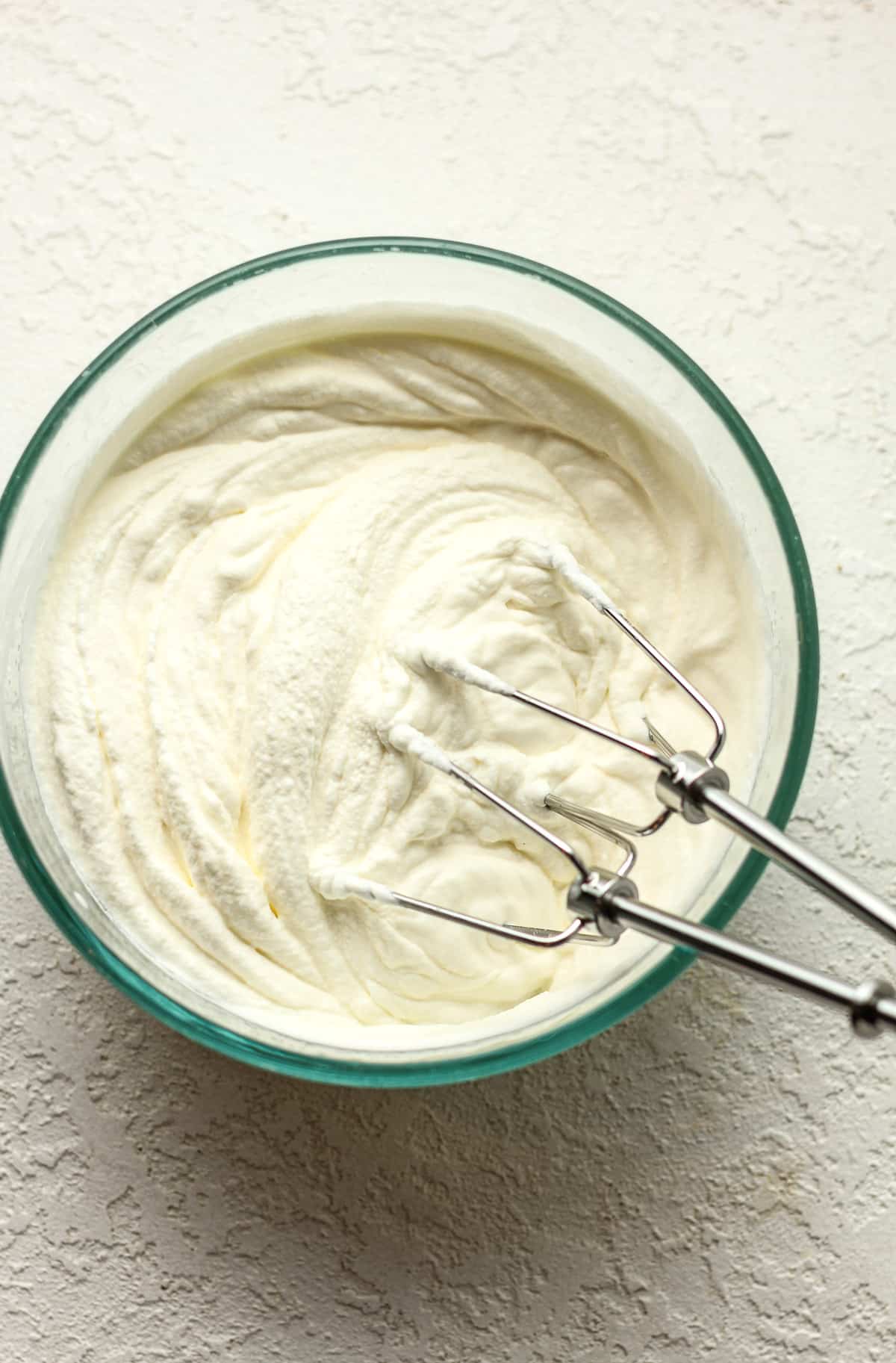 A bowl of the whipped cream with mixer tools.