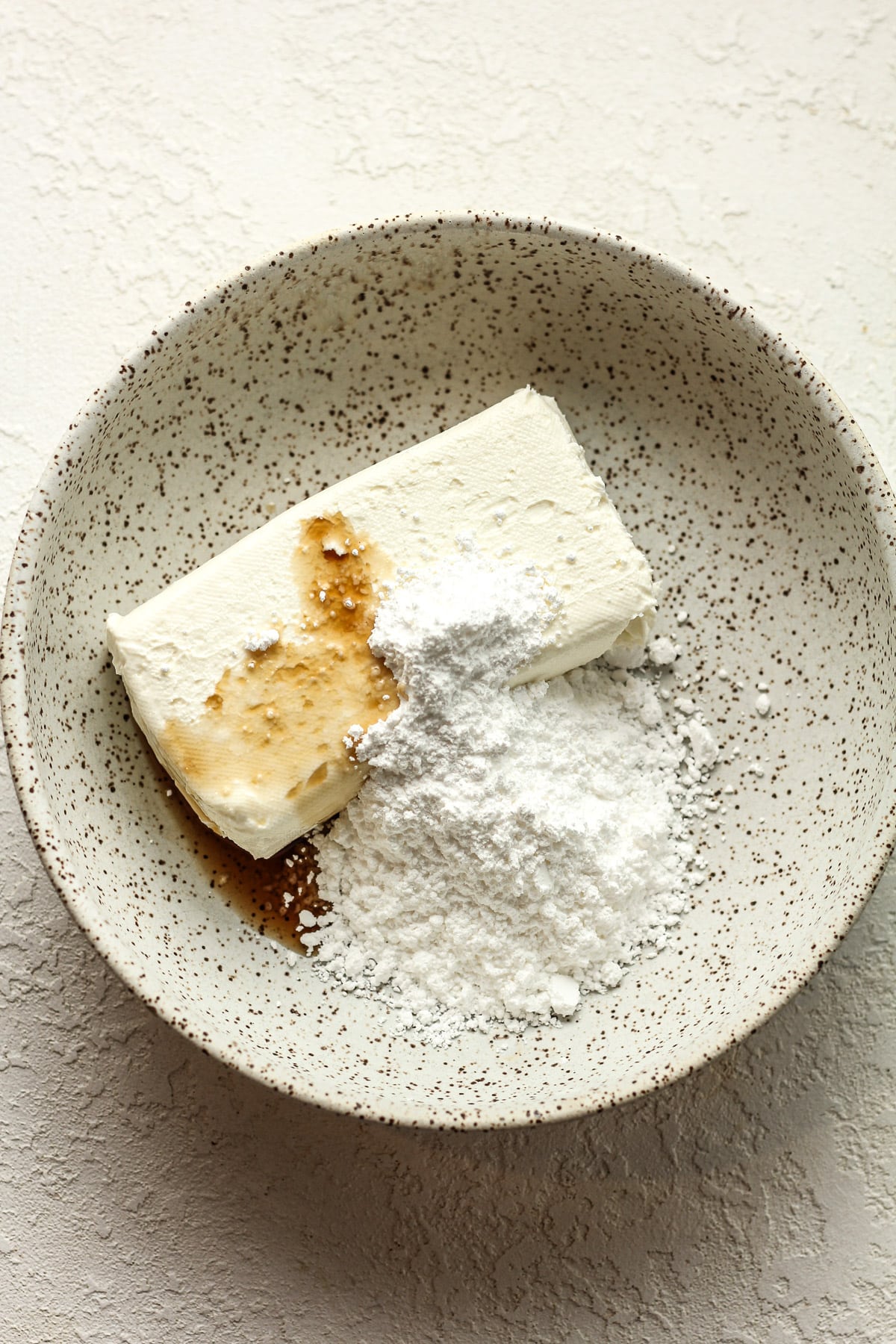 A bowl of a block of cream cheese, vanilla, and powdered sugar.