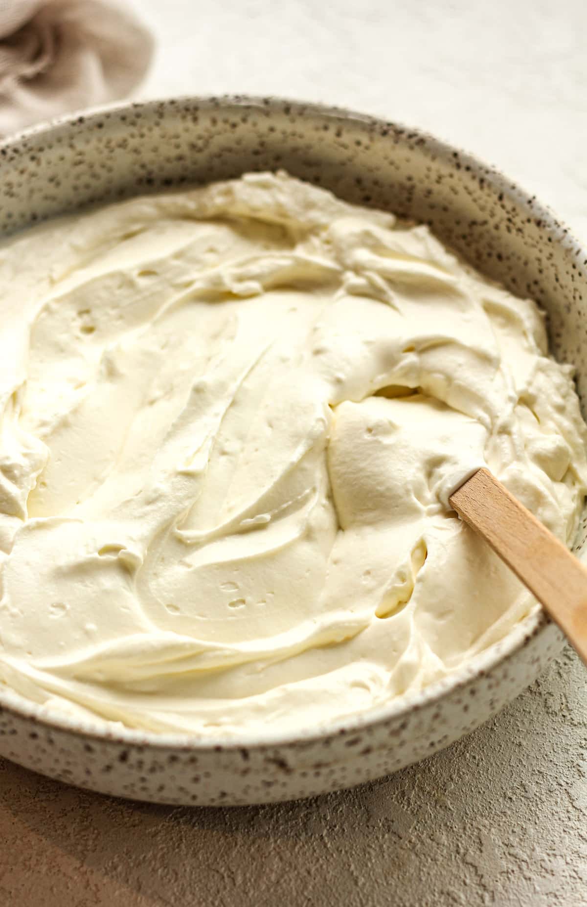 Side view of a bowl of the cream cheese filling with a spatula.