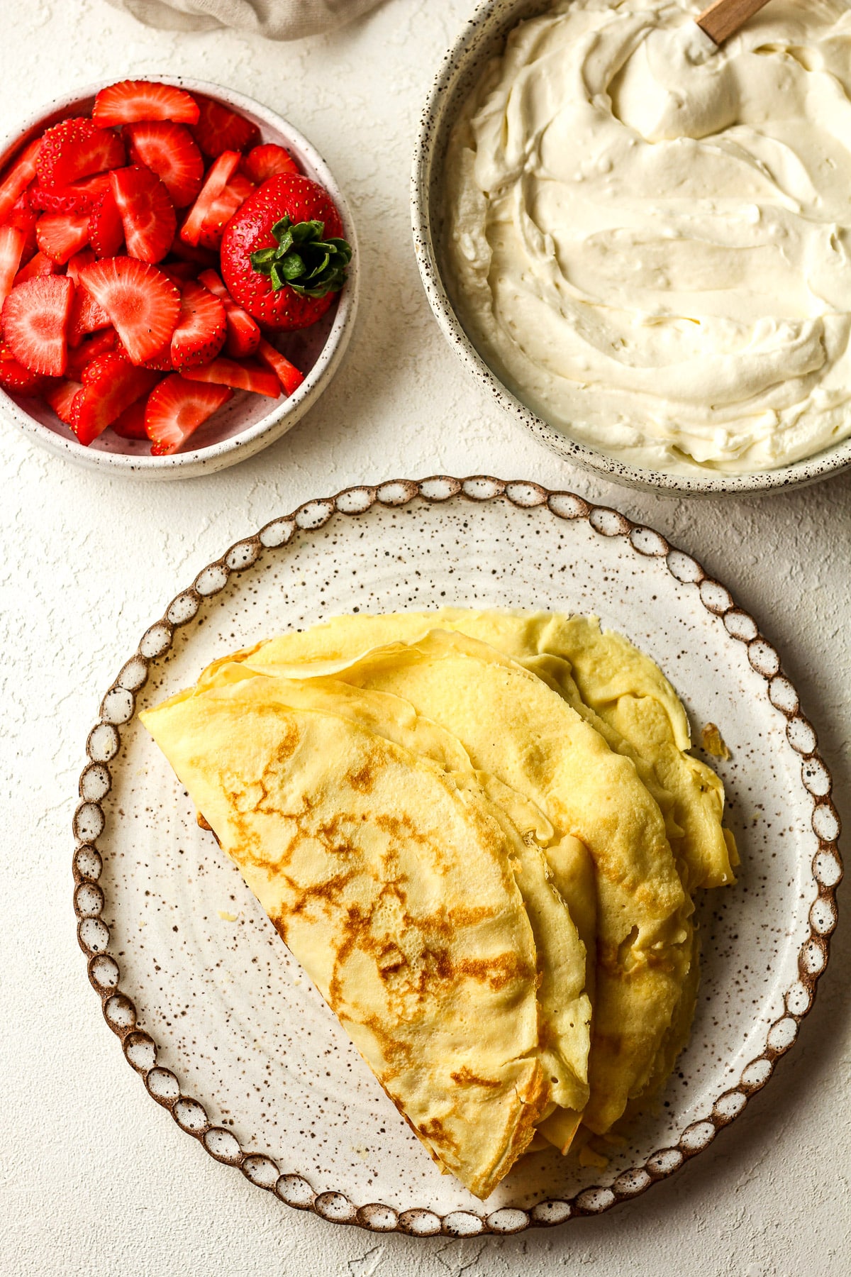 Overhead view of the thin crepes, cream cheese filling, and sliced strawberries.