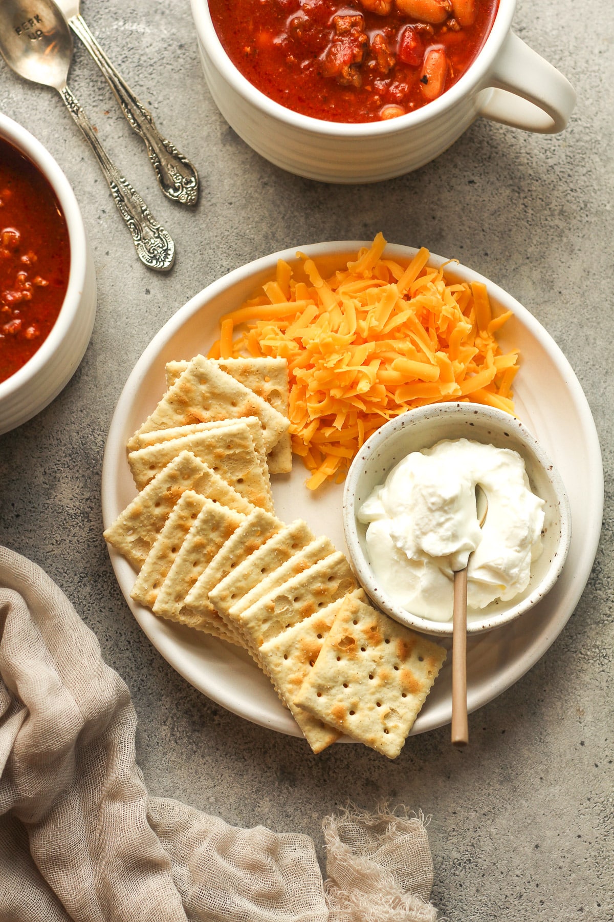 A plate of shredded cheddar cheese, saltine crackers, and a bowl of sour cream.