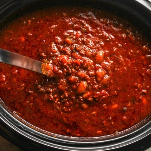 A soup ladle lifting some chili out of a slow cooker.