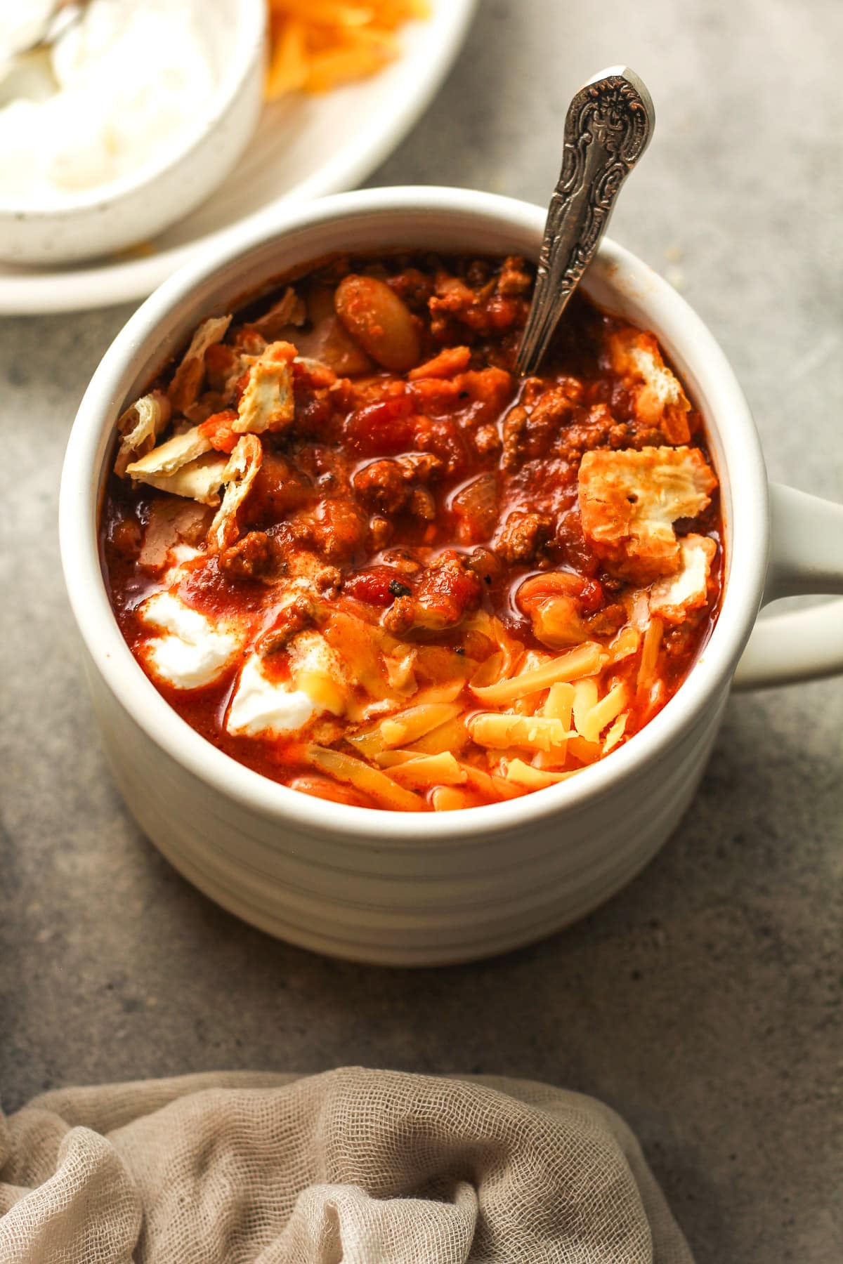 A mug of easy slow cooker chili with crackers, cheese, and sour cream.