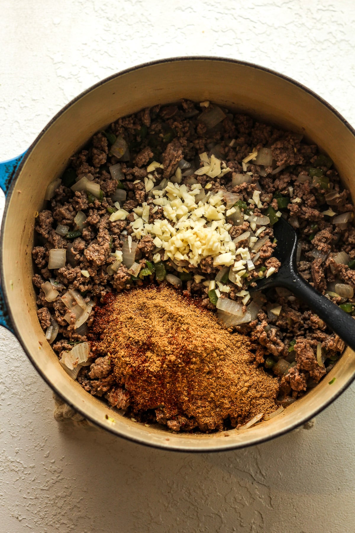 A stock pot of the browned beef mixture with garlic and seasonings on top.