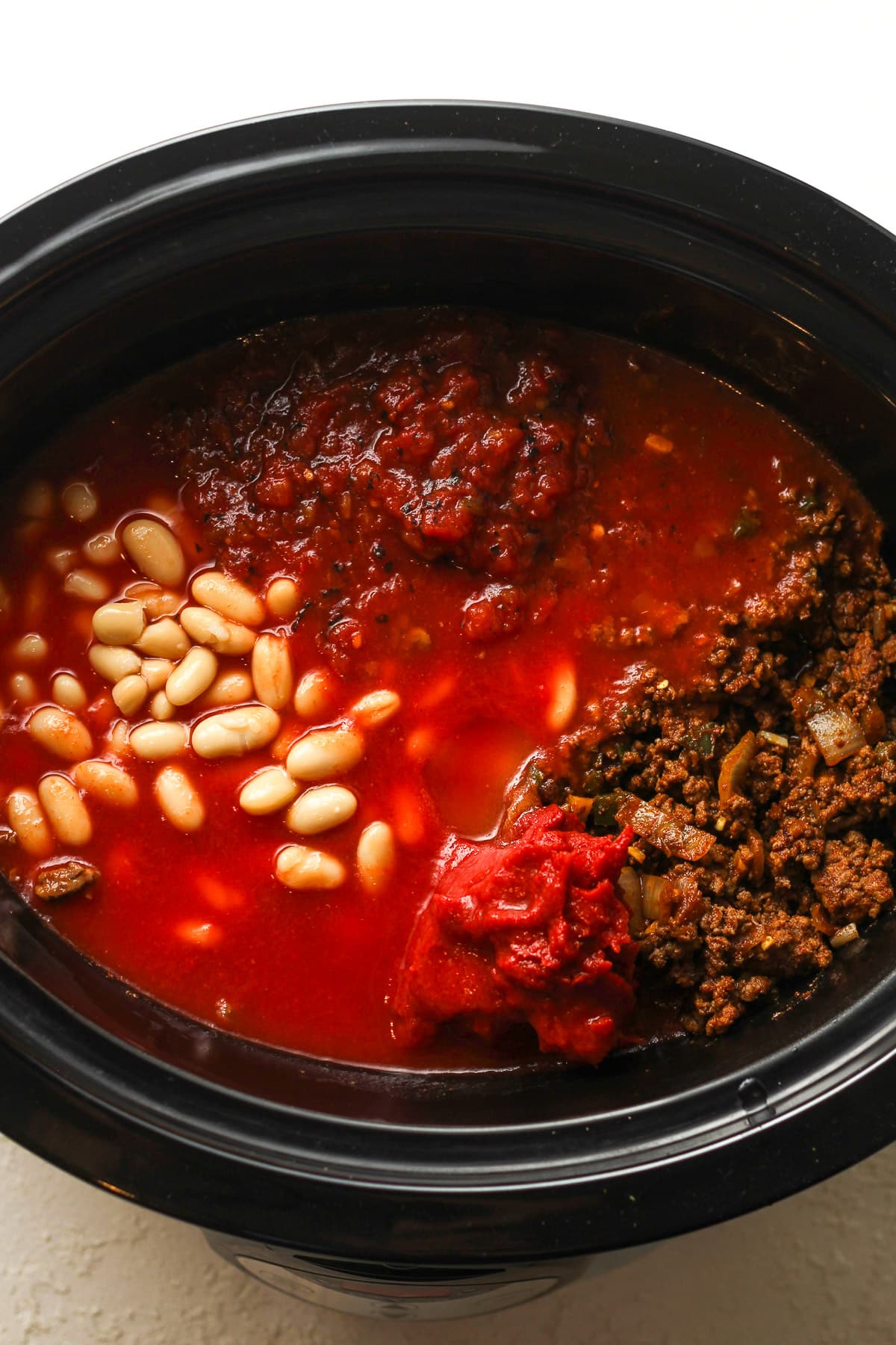 Overhead view of a slow cooker with the just added ingredients before stirring together.