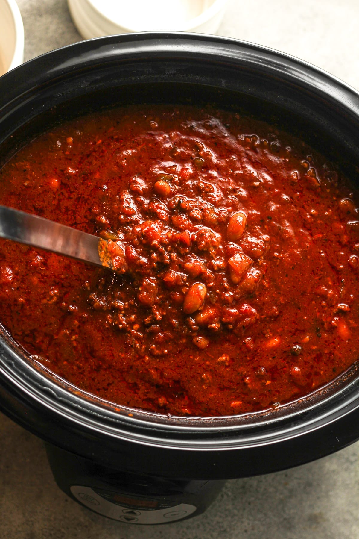 A soup ladle lifting some chili out of a slow cooker.