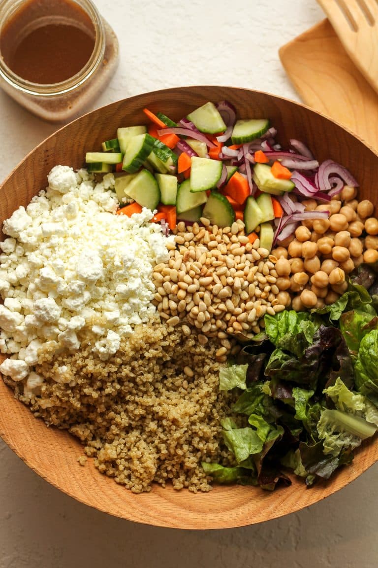 A large wooden bowl of quinoa salad separated by ingredients and a jar of balsamic dressing.