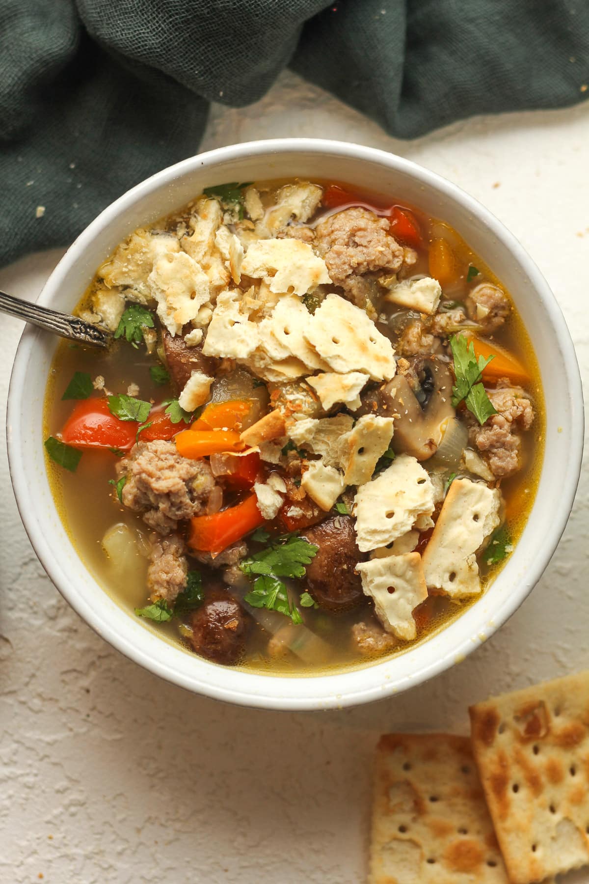 A bowl of sausage vegetable soup with crushed up crackers.