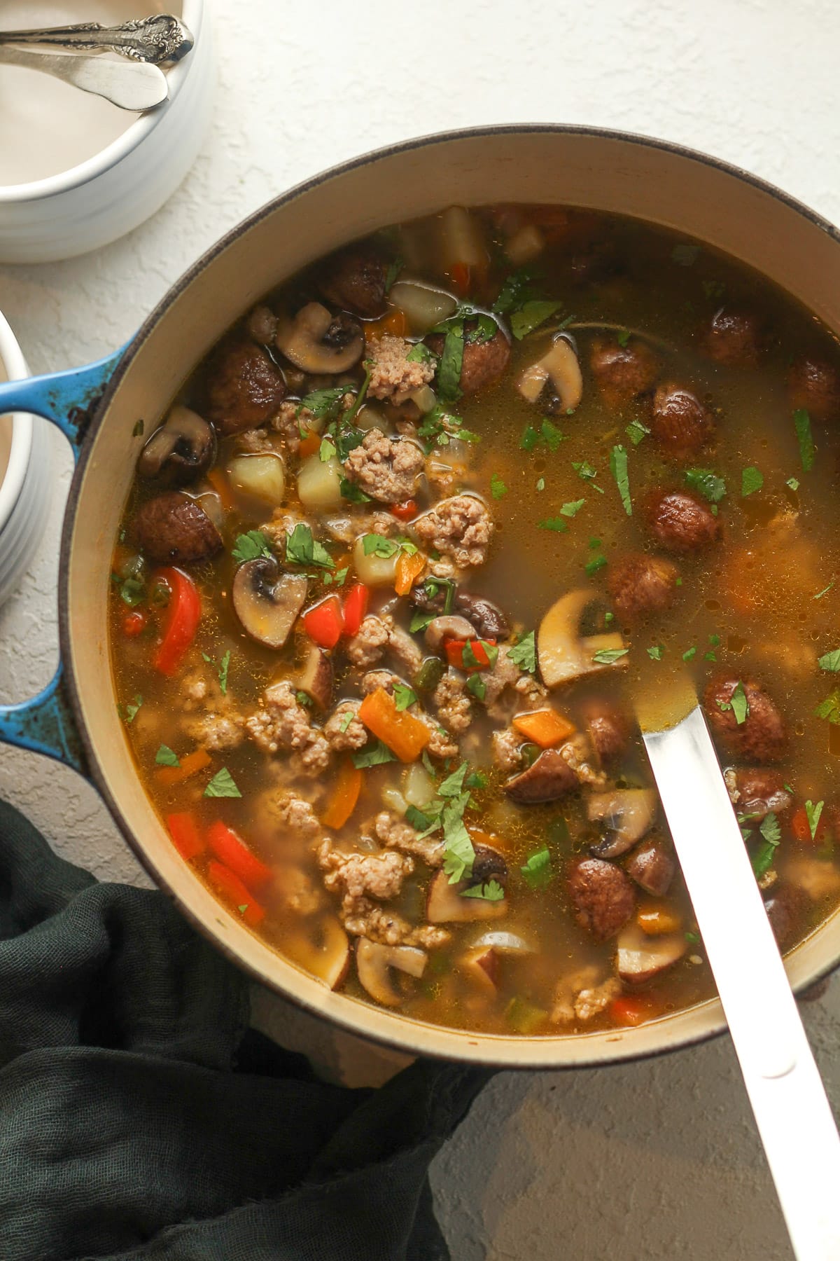 A large pot of sausage vegetable soup with a soup ladle.