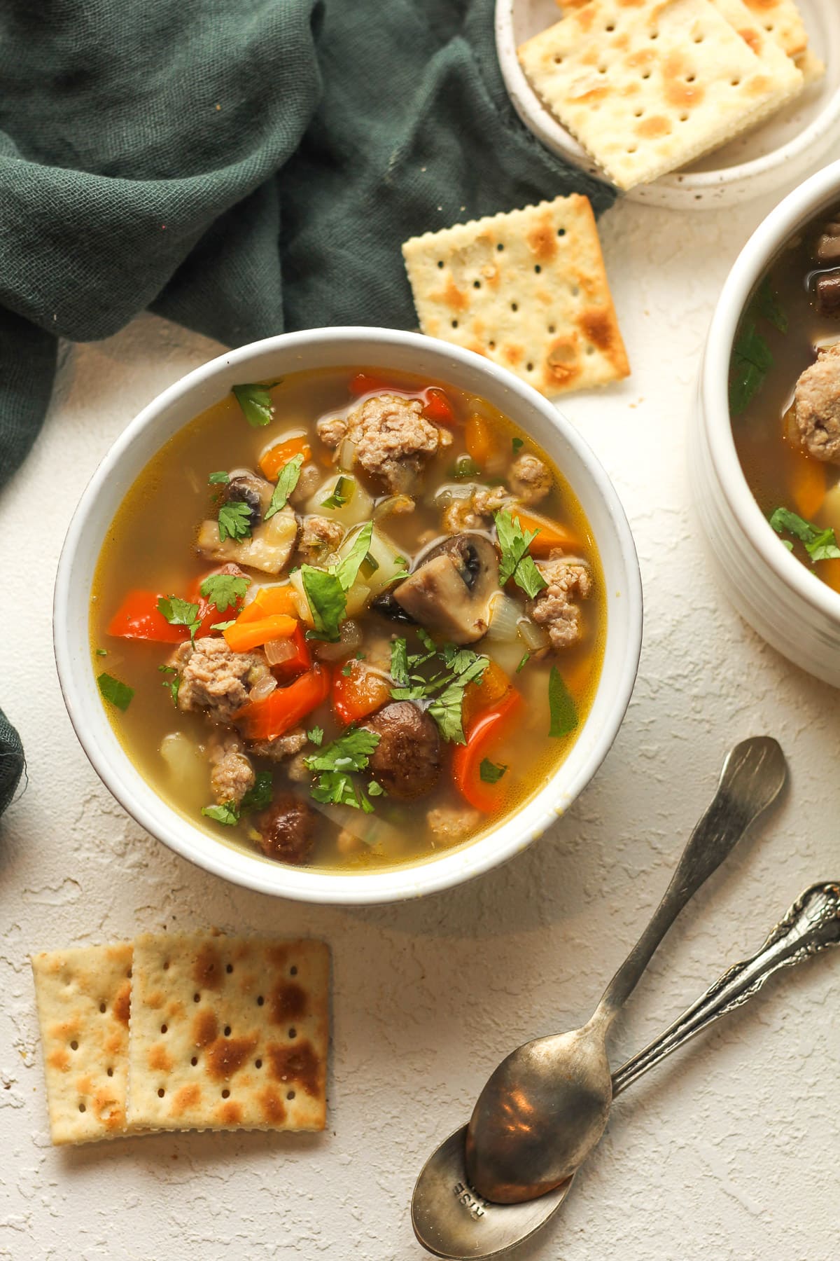 Two bowls of turkey sausage veggie soup with saltine crackers.