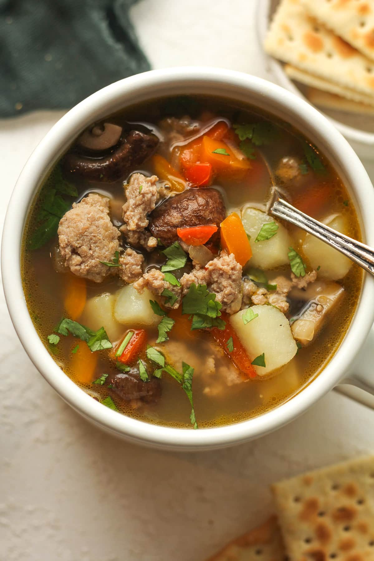 A mug of sausage vegetable soup with mushrooms.