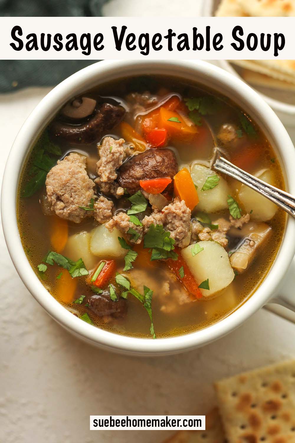 A mug of sausage vegetable soup with a spoon.