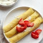 Overhead view of three rolled crepes with cream cheese and sliced strawberries.