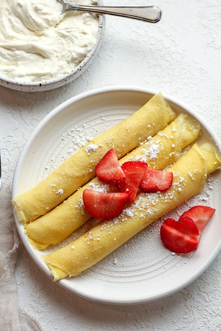 Overhead view of three rolled crepes with cream cheese and sliced strawberries.