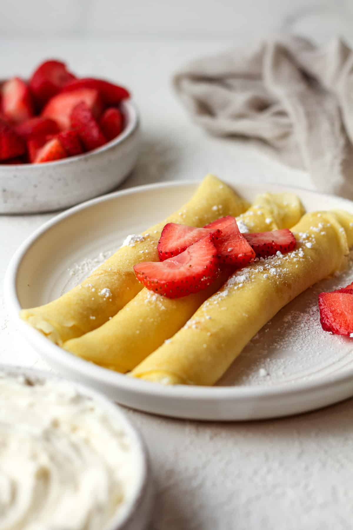 Side view of three rolled crepes stuffed with cream cheese filling and topped with strawberries.