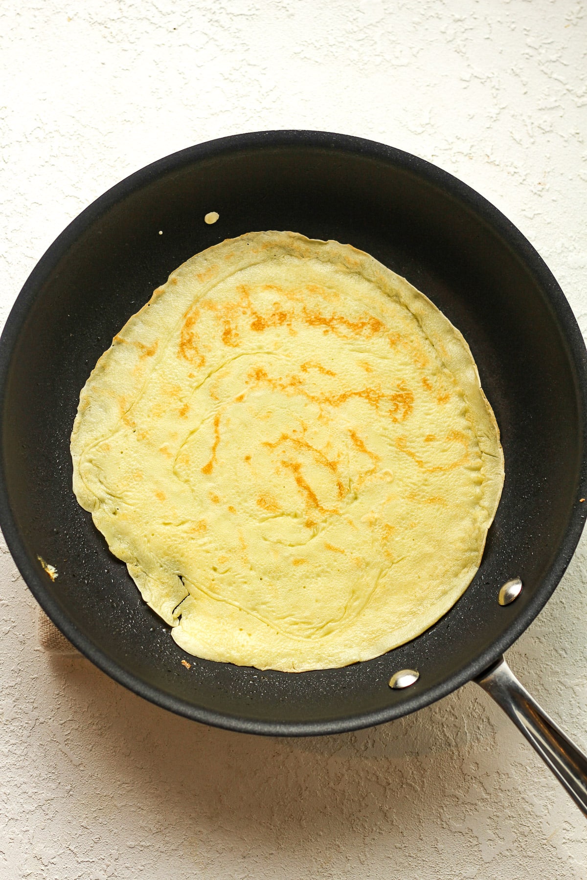 A pan with a thin crepe cooking.