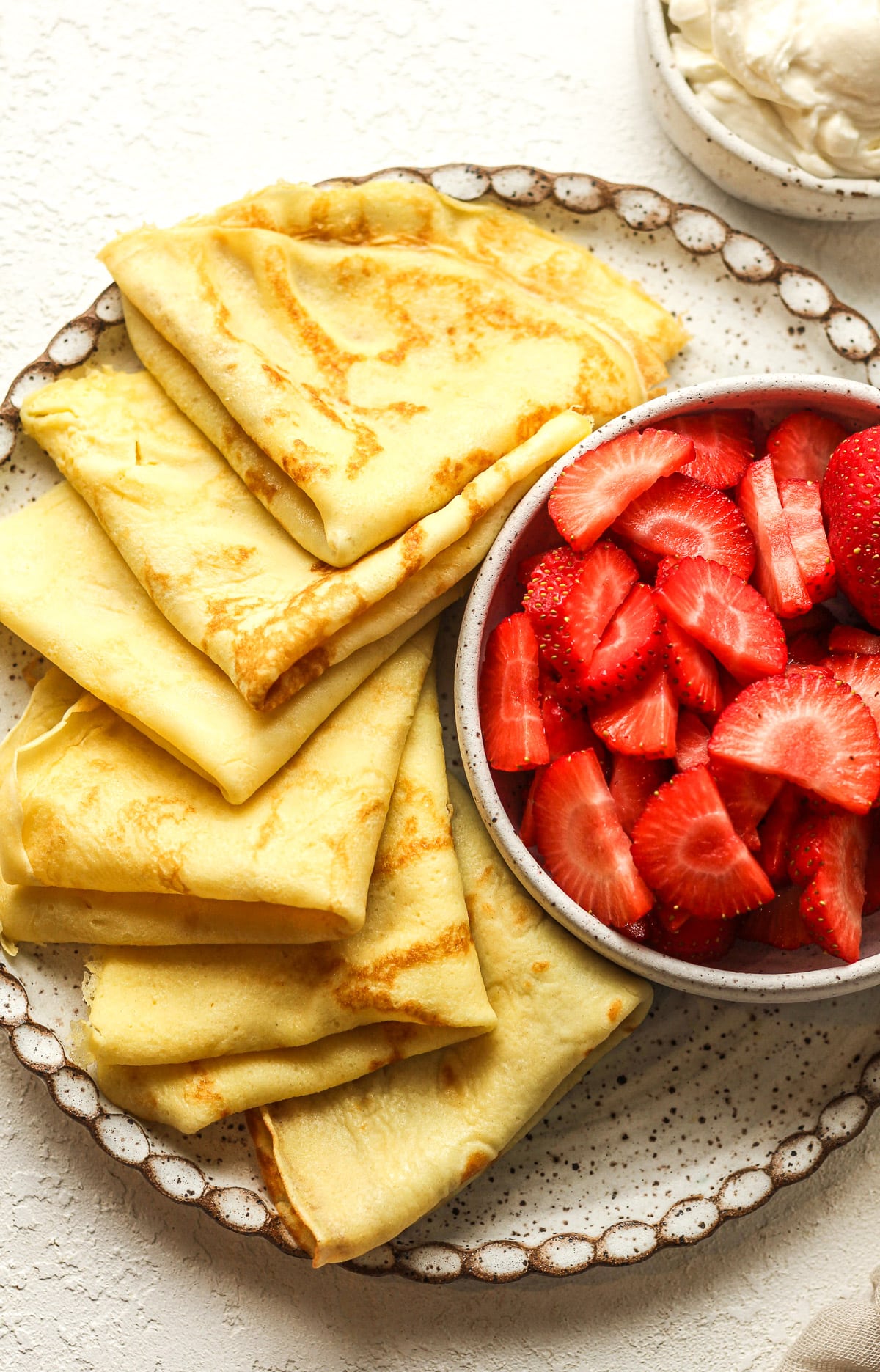 Closeup on a plat of folded crepes and a bowl of sliced strawberries.