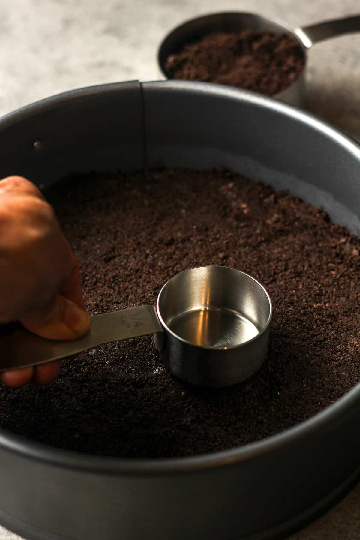 A hand pressing a measuring cup down on the Oreo crust.