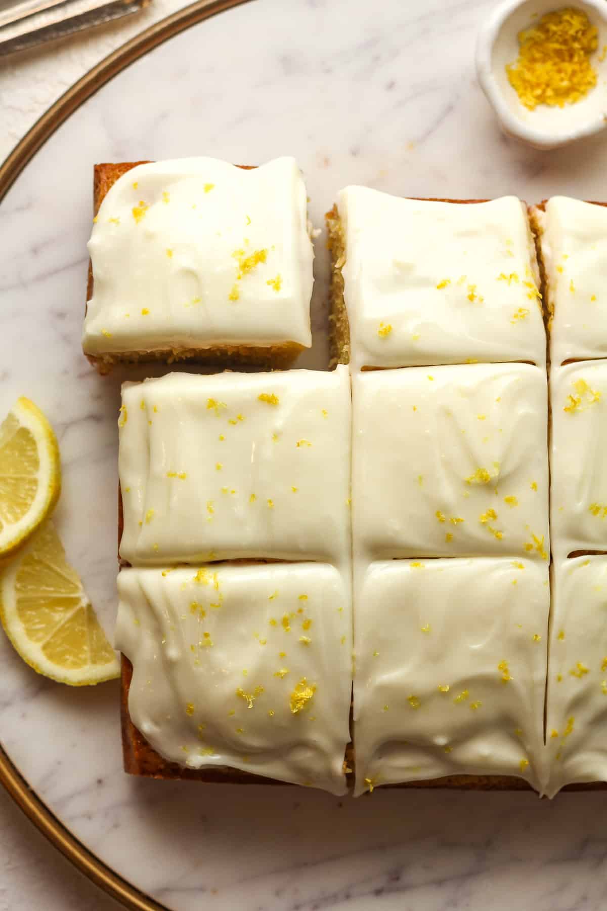 A round platter of sliced lemon cake with creamy cheese frosting topped with zest.