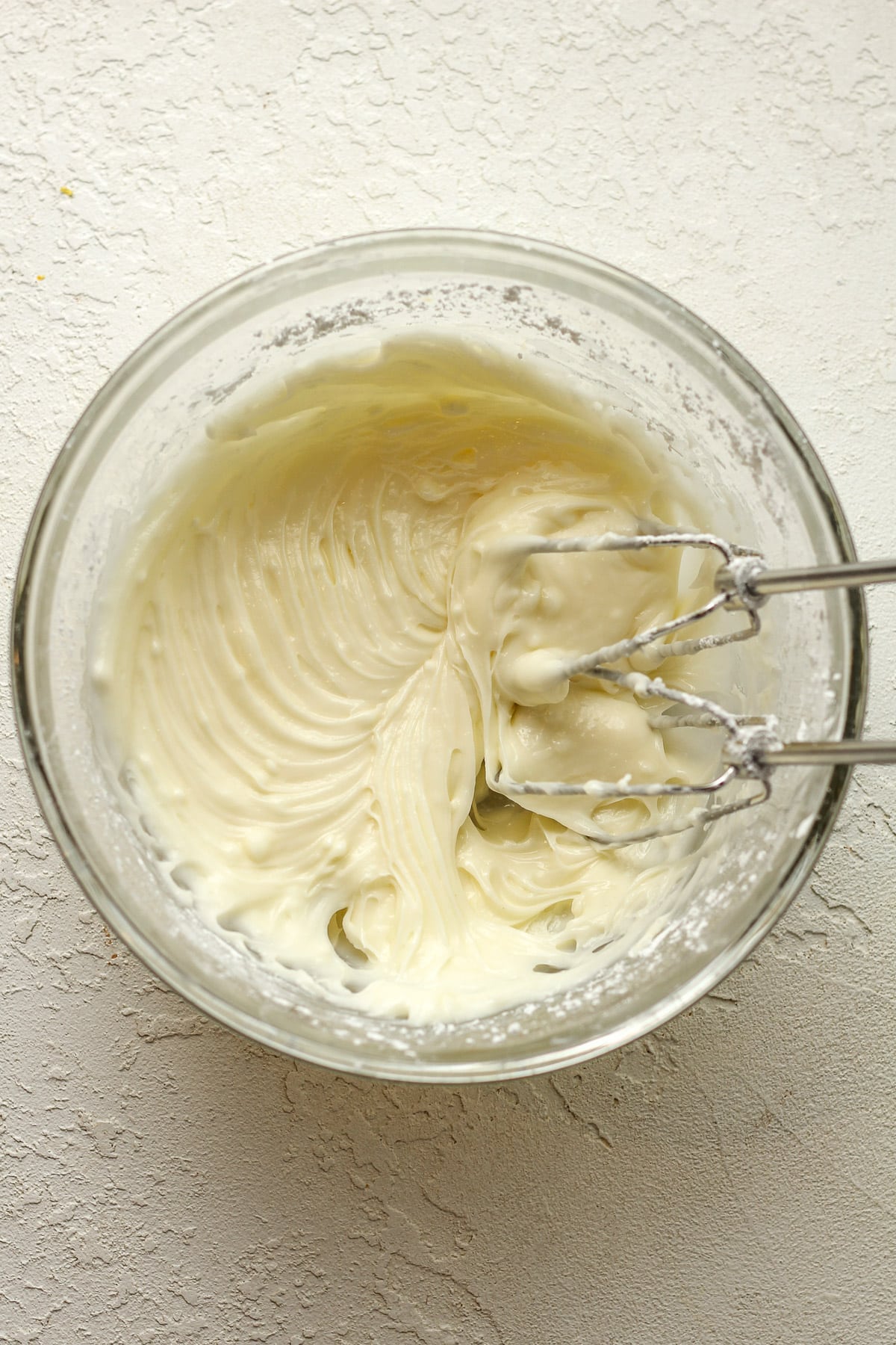 A bowl of the cream cheese icing with mixer paddles.