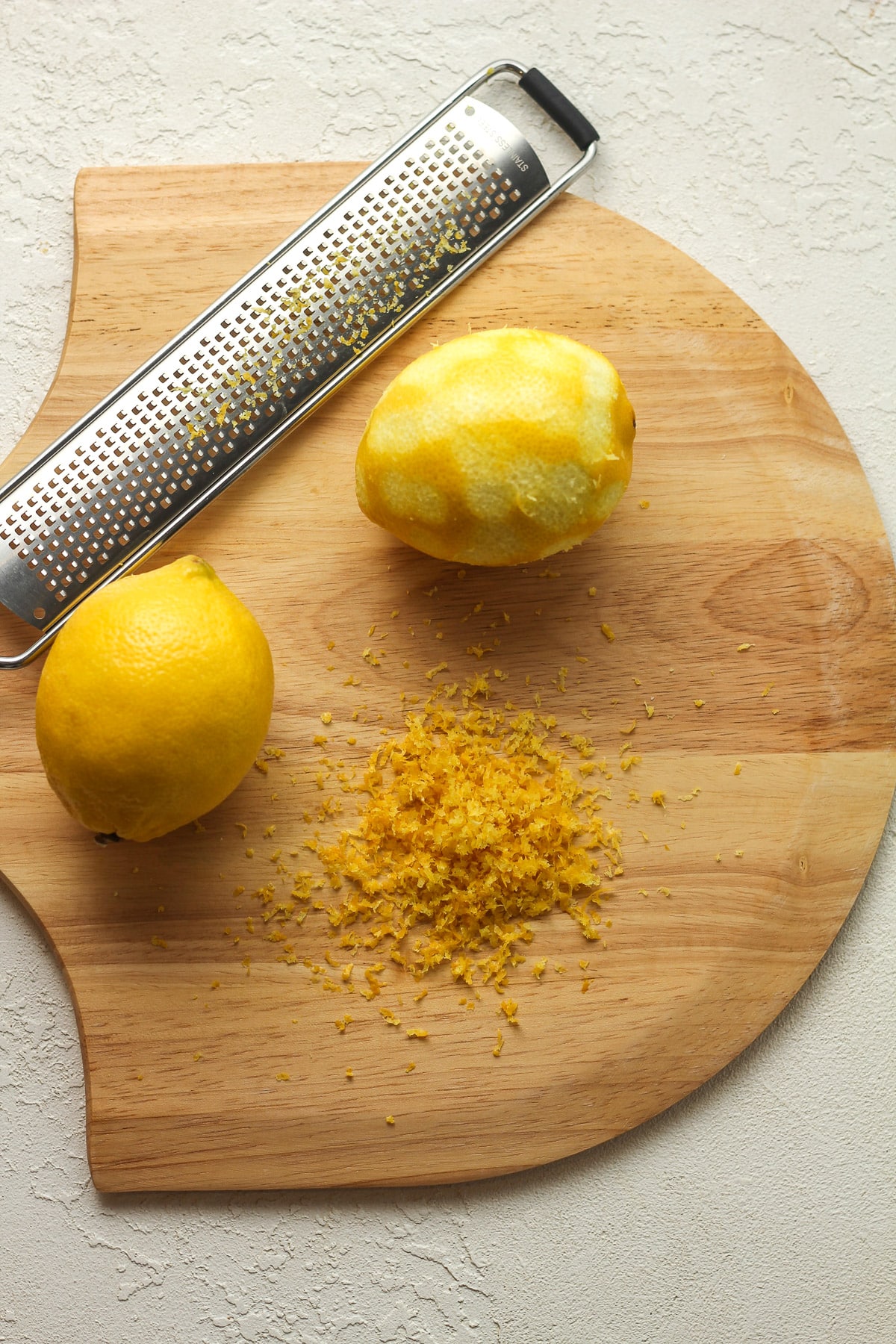 Two lemons on a board with one zested and a microplane next to it.