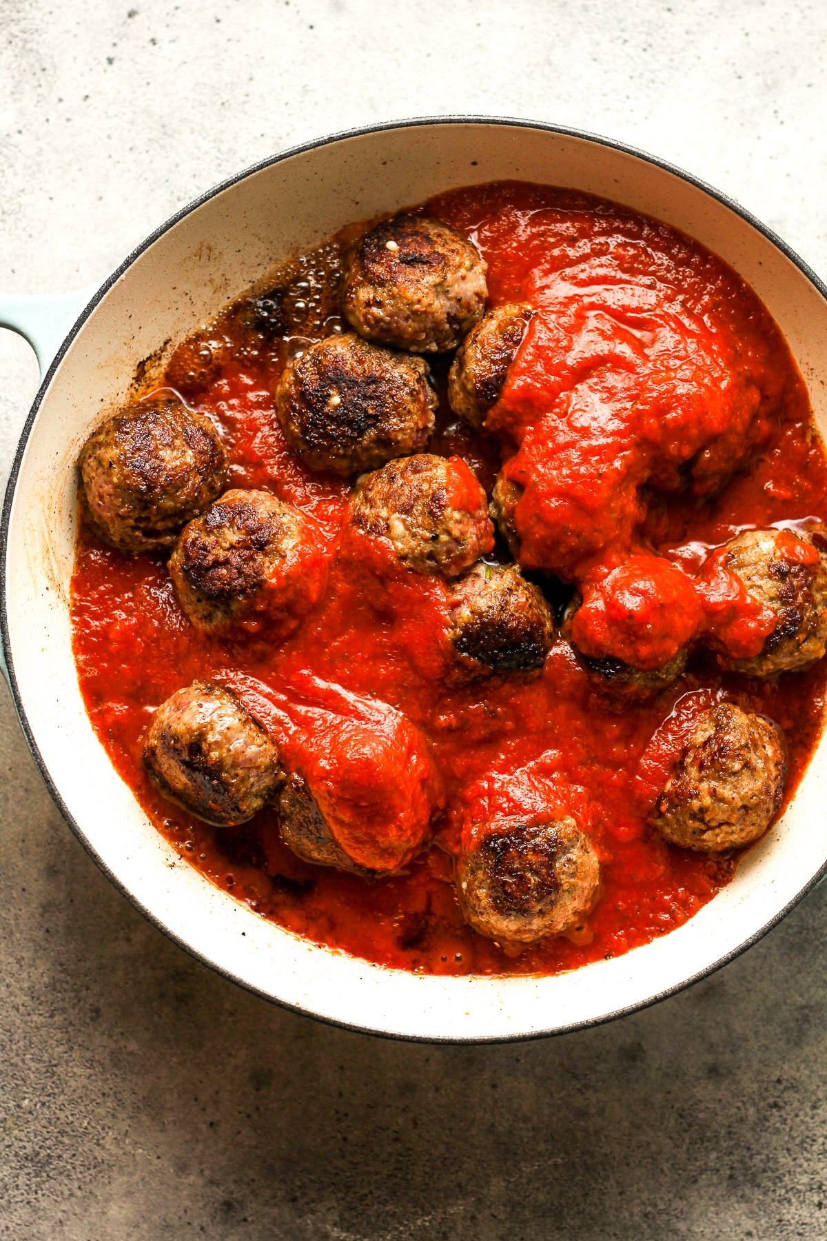 A pan of the browned meatballs topped with some marinara sauce.