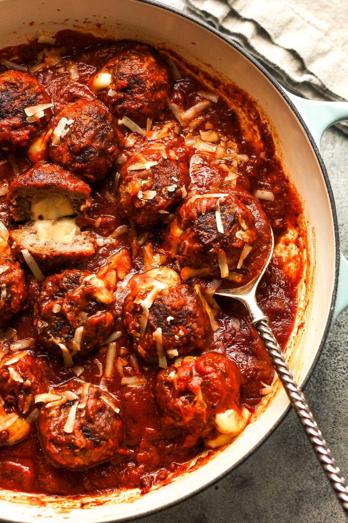 Overhead shot of a partial pan of cheese stuffed meatballs with a serving spoon and one meatball sliced open.