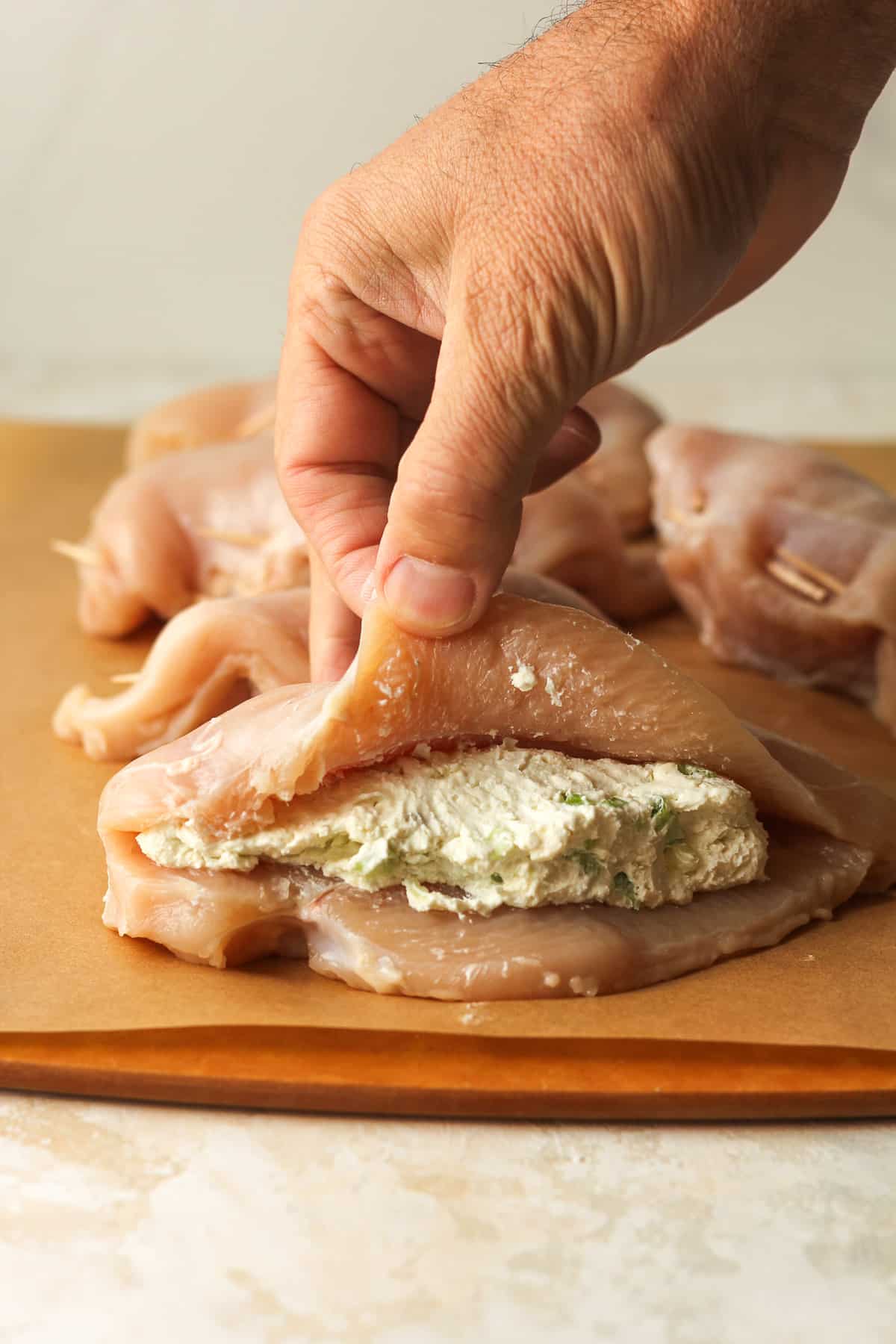 A hand pulling up the top part of the raw chicken breast showing the cream cheese stuffing inside.