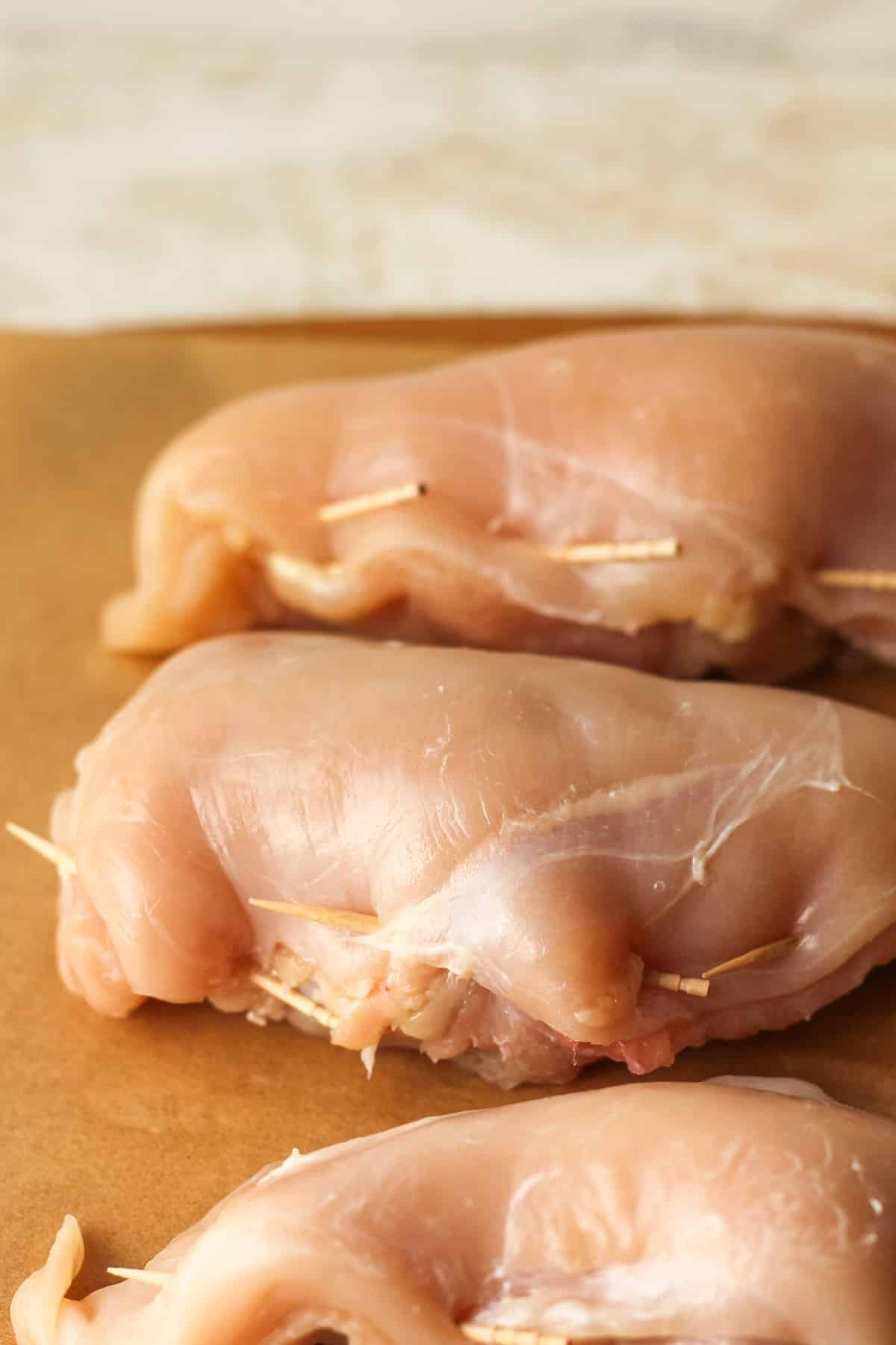 Side view of some raw stuffed chicken breasts with toothpick holding the outsides together.