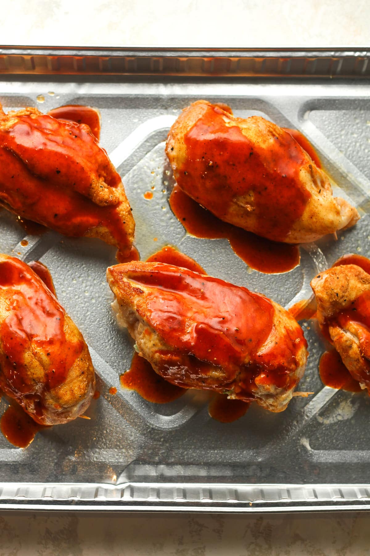 A disposable pan with the prepped breasts after searing, topped with buffalo sauce.